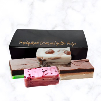 One black box of fudge with bars of fudge stacked in front of the boxes, all displayed on a white marble background