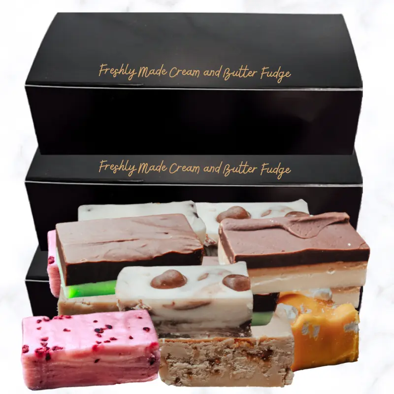 Three boxes of Fudge Three black boxes of fudge with bars of fudge stacked in front of the boxes, all displayed on a white marble background